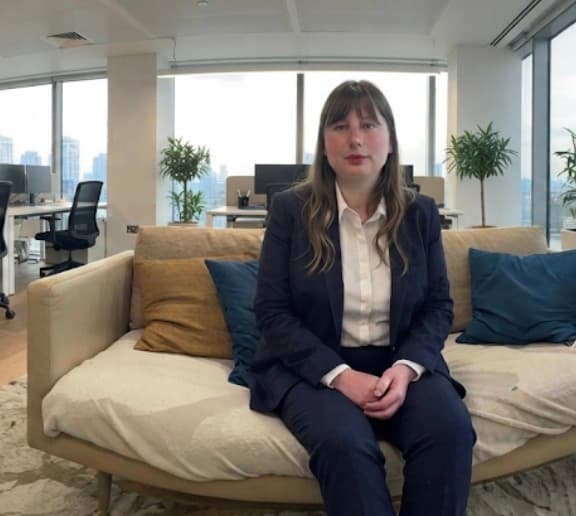 Woman in a navy suit sits on a beige couch in a bright, modern office.