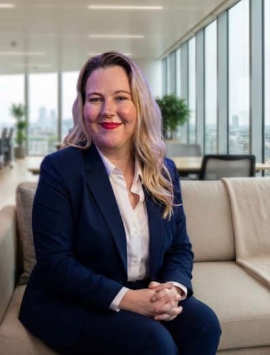 Professional woman in a navy blazer sitting on a couch in a bright modern office.